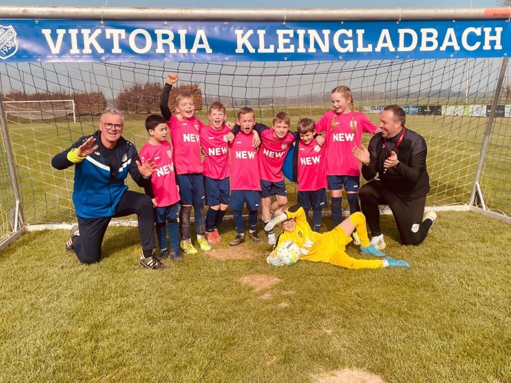E-Junioren in pinken Trikots jubeln mit ihren beiden Trainern vor dem Vereinstor