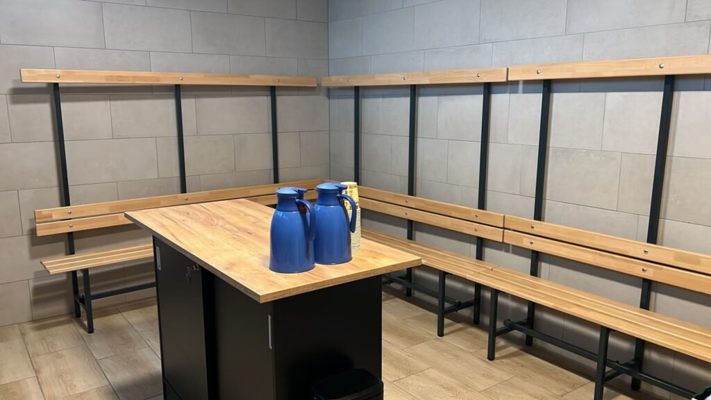 Gästekabine mit neuen Holzbänken, Garderobe und einem Tisch mit blauen Thermoskannen