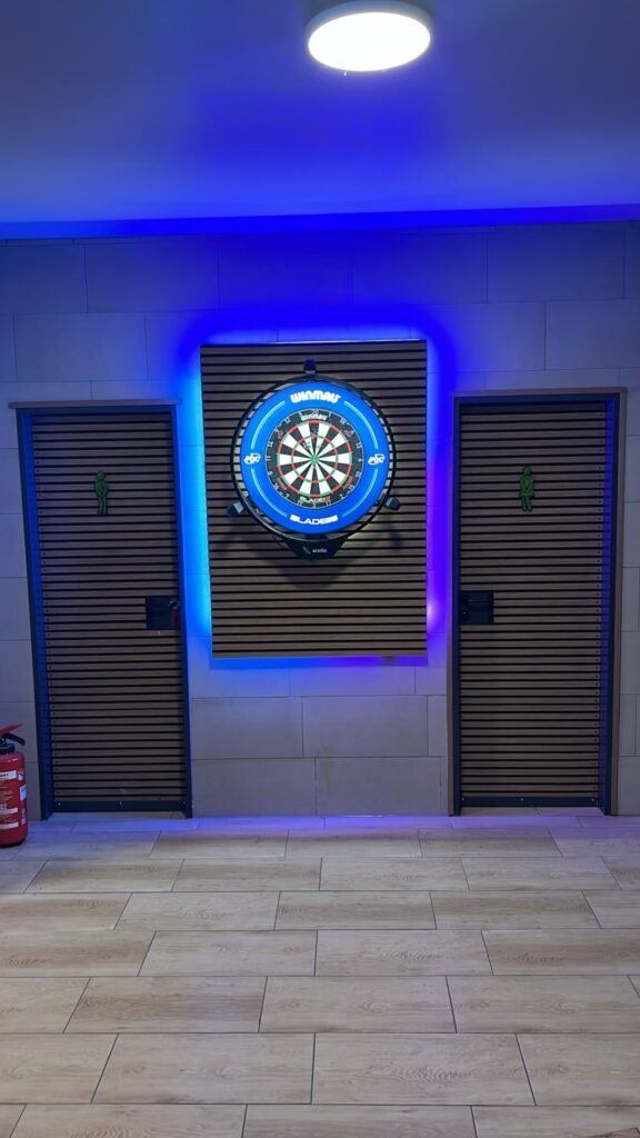 Dartscheibe mit blauer Beleuchtung auf einer Holzlamellenwand im Vereinsheim